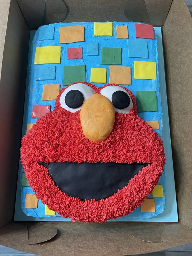 Elmo birthday sheet cake with red buttercream fur on a background of colorful squares